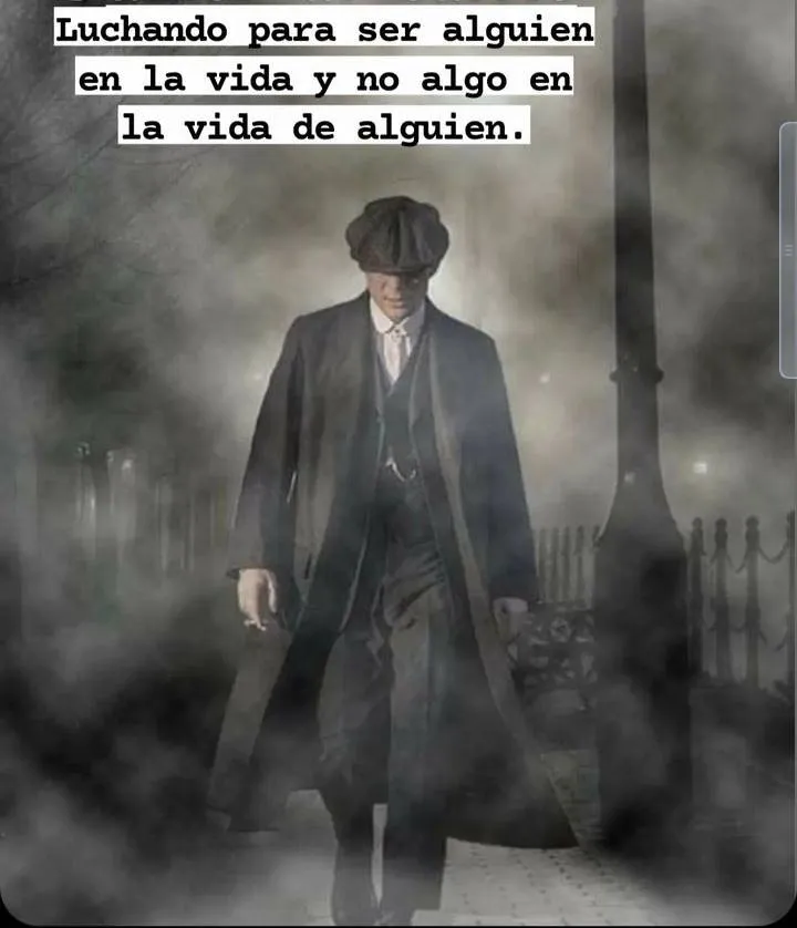 Un hombre vestido con ropa de época camina por una calle oscura y foggy. Lleva un abrigo largo y un sombrero, y sostiene un cigarrillo en la mano. La expresión de su rostro es seria y determinada.